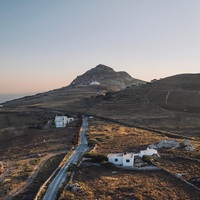 Σκηνή πρώτη. Το πλοίο προσεγγίζει το λιμάνι της Τήνου και ο βράχος του Εξωμβούργου είναι σαν φάρος, από παντού φαίνεται κι ας μην αναβοσβήνει, ήσυχα υποδέχεται, παρακολουθεί, καθοδηγεί.

Σκηνή δεύτερη. Αρχίζει να πέφτει ο ήλιος και στη διαδρομή από Μέση προς Ξώμπουργο, η τηνιακή φύση, αναλόγως την εποχή, άλλοτε προσφέρει παπαρούνες και μαργαρίτες, άλλοτε  στάχυα. Κάπου εκεί κι εμείς, με ανοιχτά συνήθως παράθυρα και μουσική τύπου «πάμε να κατακτήσουμε το Έβερεστ» είναι σαν να παίζουμε σε διαφημιστικό σποτ αυτοκίνητου με φόντο ένα άλλο Mont-Saint-Michel. 

Σκηνή τρίτη. Παρκάρουμε το αυτοκίνητο στην Ιερή Καρδιά (υπάρχει πιο ωραίο όνομα αφετηρίας;) Από εδώ ξεκινάει η ανάβαση, το τοπίο θυμίζει Lord of the Rings: πετρόχτιστα μονοπάτια, απομεινάρια καστροπολιτείας και μύθοι για μυστικά περάσματα που αν μπεις μπορεί να μην ξαναβγείς. 

Σκηνή τέταρτη. Φτάνουμε στην κορυφή του βράχου, πάνω, στο σταυρό. Είμαστε drowns με χέρια και πόδια. Αν έχει σύννεφα θα δούμε τους πρόποδες του Τσικνιά (όχι κι άσχημα). Αν πάλι έχει ορατότητα θα μετρήσουμε νησιά: σχεδόν όλες οι Κυκλάδες, Ικαρία, Χίος ,Ψαρά, αχνά η Ανατολική πλευρά της Αττικής, η Εύβοια και όπως λέει ο μπαμπάς Σάββας, αν προσέξεις καλά, φαίνεται και ο Πύργος του Άιφελ.

Στην επιστροφή, κλειστές οι μουσικές, κλειστά και τα στόματα. Ο βράχος χωρίς να πει κουβέντα, είπε αρκετά για το υπόλοιπο της μέρας. Πύργο Άιφελ δεν είδαμε αλλά αρκεί που ξέρουμε ότι είναι κάπου εκεί, στον βάθος του ατελείωτου ορίζοντα. 

Τα σανδάλια #exomvourgo εμπνέονται από τις παραπάνω σκηνές και από άλλες που δεν χωράνε εύκολα σε κείμενο μιας ανάρτησης στο instagram.